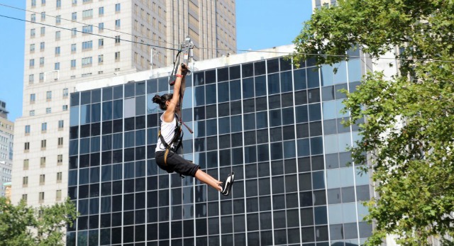 A woman zip lines in front of an office building at NYC's Summer Streets.
