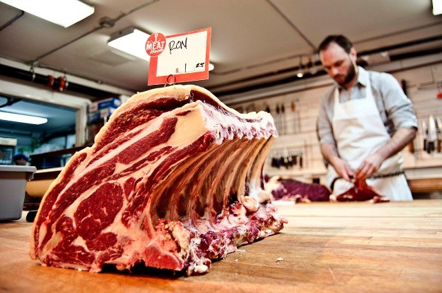 Image of a large set of ribs, in the backgroun a man prepares meat for cooking.