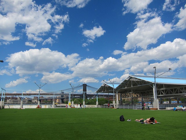 Image of a Brooklyn bridge park with a man sunbathing on the lawn on a beautiful day with bright blue skies