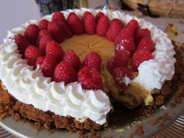 Image of the top of a passion fruit pie decorated with whipped cream around the edges and large raspberries