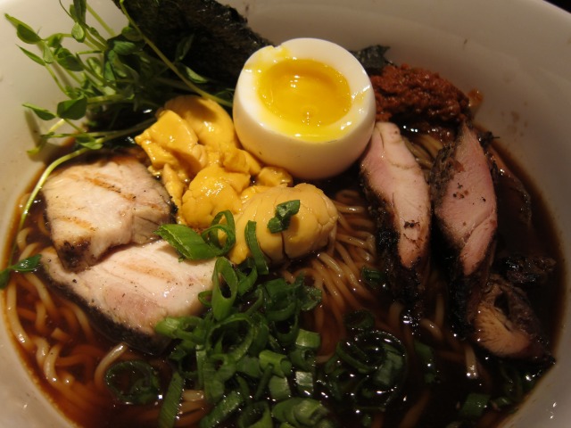 A bowl filled with pork veggies, scallions, and ramen noodles in a dark broth.