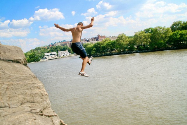 A young man jumping off of a rock into a the Hudson River