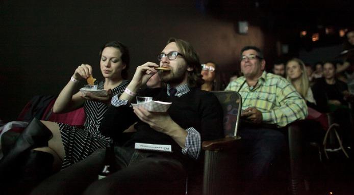 Theater-goers eating food inside a movie theater while watching the screen at the NYC Food Film Festival
