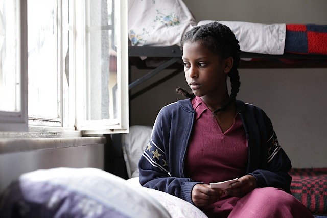 A young lady sits on a bed looking out of the window in a scene from the movie Difret