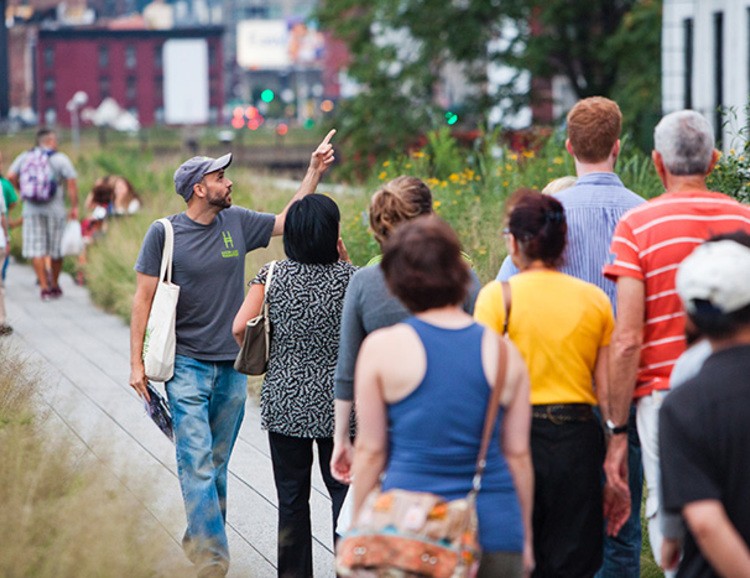 Man giving a tour of the High line in New York City pointing upwards at a building.