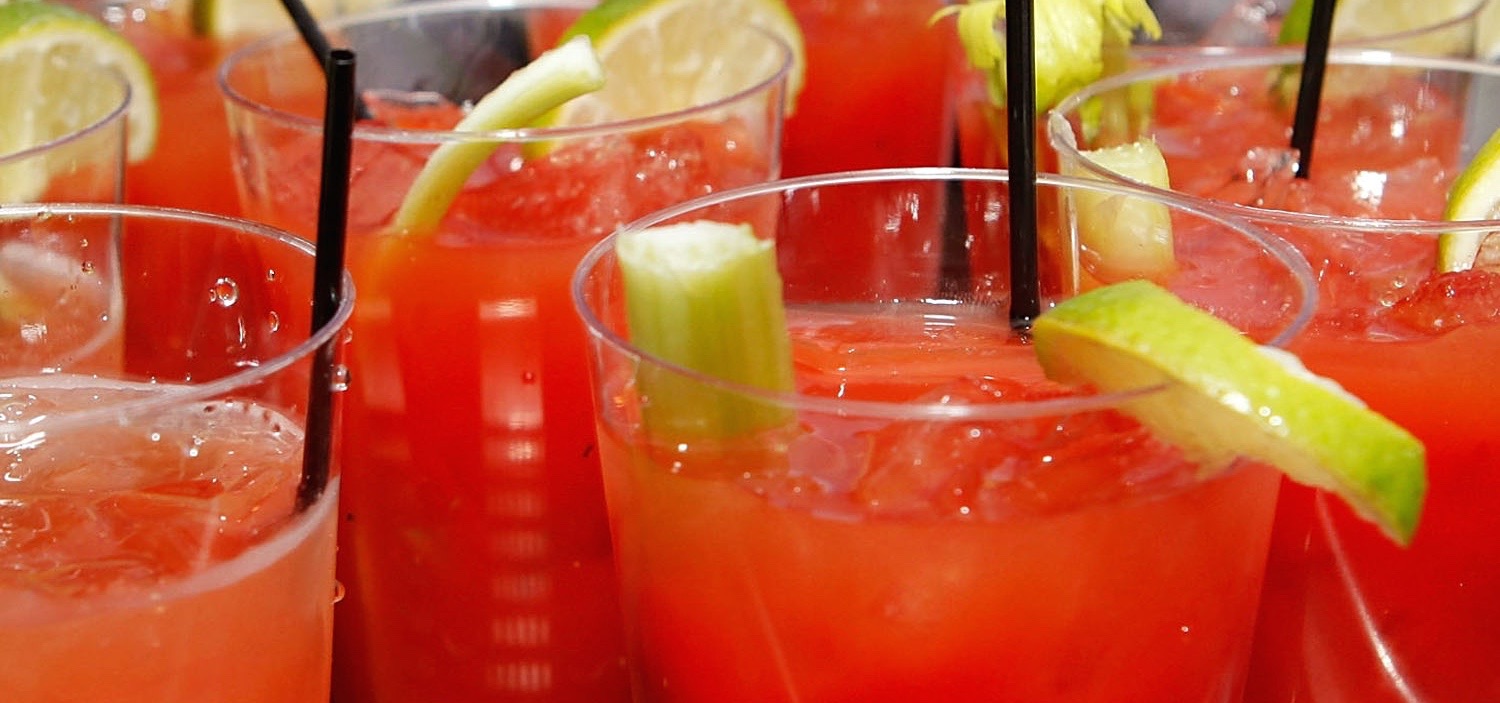 A zoomed in view of Bloody Mary's side by side with celery and lime garnishes and black straws.