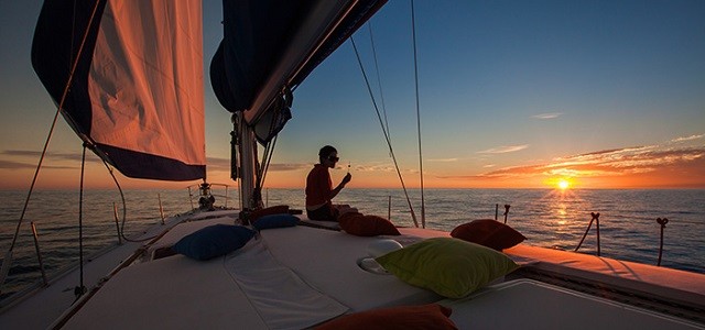 A person sitting on a sailboat with the sunset in the background 