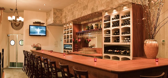 The Tangled Vine Wine Bar and Kitchen's dimly lit indoor restaurant with wooden bar top and bottles of wine.