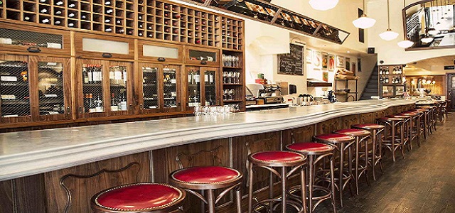 An brightly lit interior view of Vin Sur Vingt's bar top with red leather stools and wooden wine bottle shelves.