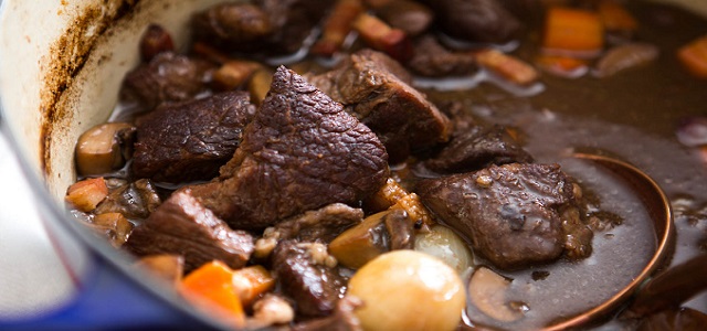 A large pot of French beef bourguignon with carrots, onions, and beef cooking.