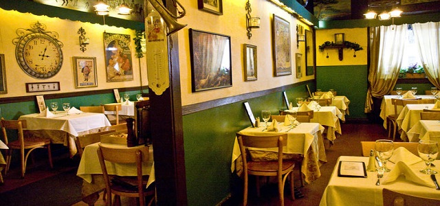 An interior view of the French bistro Chez Napoleon in New York City with linen tables, dim lights, and bright sunshine coming through windows.