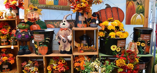 A display of fall themes crafts and decorations with colorful autumn leaves and flowers with pumpkins at an outdoor fall festival.