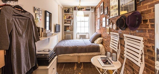 The inside of a small apartment bedroom, furnished with photographes, shelves, chairs and a bed, in New York City