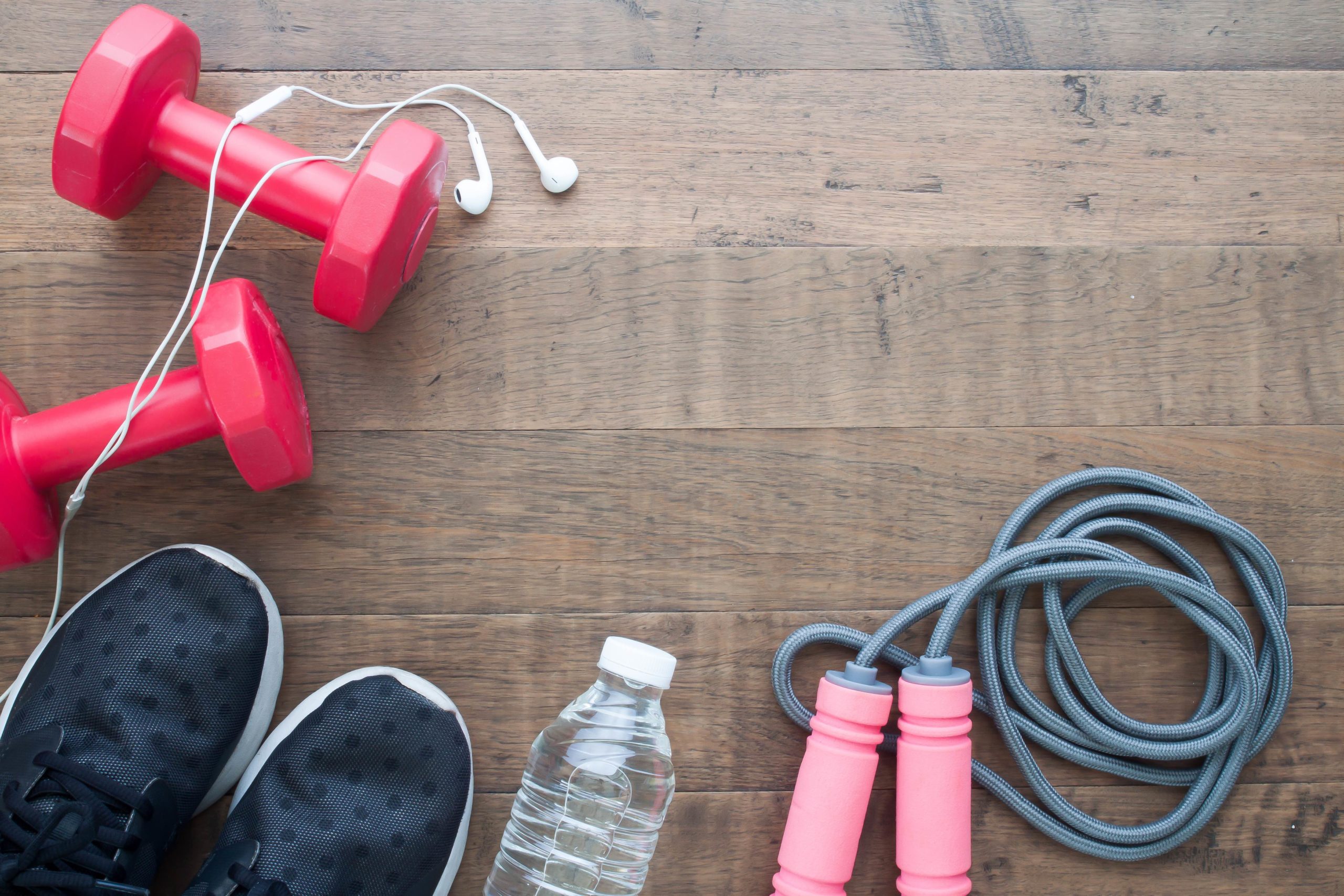 Sneakers, water bottle, jump road, dumbbells, headphones all on a wood floor ready for a home exercise