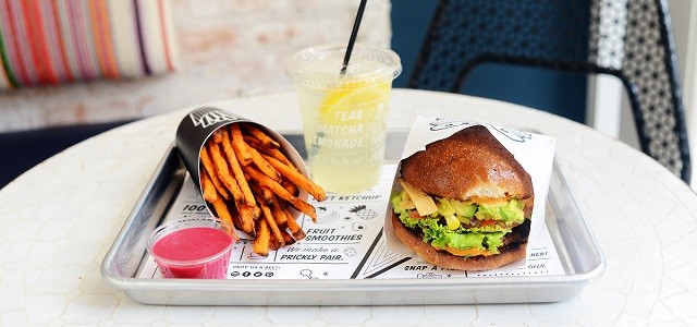 A vegetarian burger, fresh squeezed lemonade and sweet potato fries on a silver tray on a white granite table top.