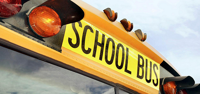 The front of a yellow school bus with bright red lights flashing and a large windshield under a school bus sign.