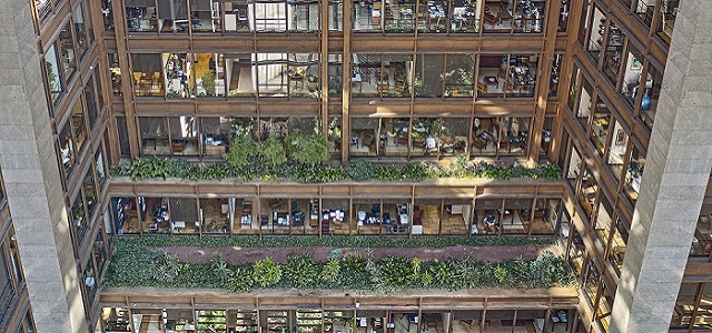 An aerial view of a tall New York City skyscraper with lots of bright windows and green plans growing on the side.