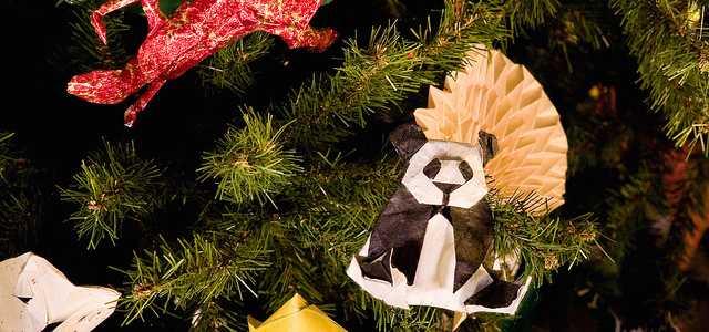 An origami white and black panda ornament on a bright green Christmas tree at the Museum of Natural History.