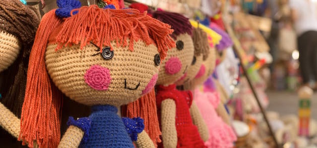 A line of dolls hanging on display at a toy store with orange and brown hair and rosy cheeks.