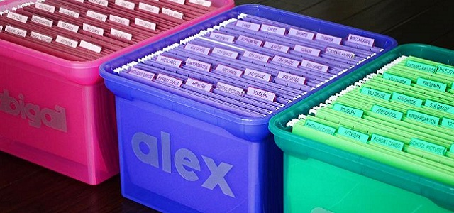 Three brightly colored plastic containers labeled with names to sort mail or other paper documents.