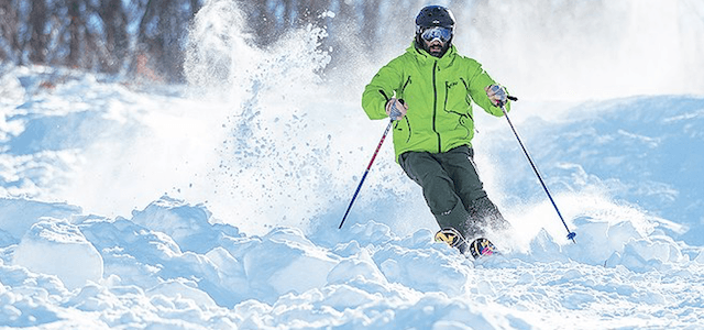 A skier wearing a bright neon green jacket racing down a snow covered mountain trail with a black helmet and goggles.
