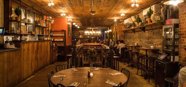 An interior view of The Smile's dimly lit bar and dining tables with rustic exposed brick and wooden floors.