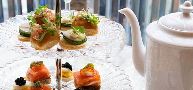 Fresh and colorful finger sandwiches on a glass platter with a white tea pot.