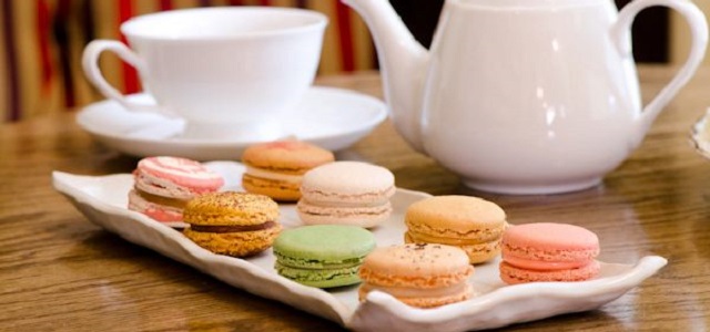 Colorful macaroons and a white tea pot sit on a wooden table at Bosie Tea Parlor in NYC.