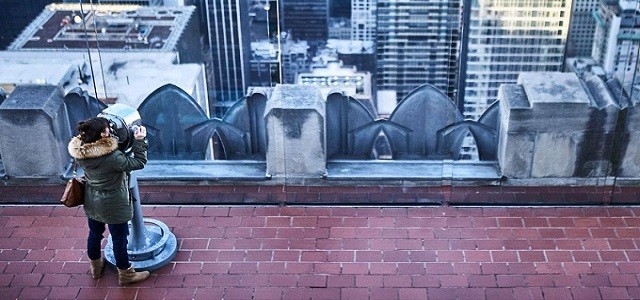 A women on top of the Empire State Building overlooking New York City on a cloudy day.