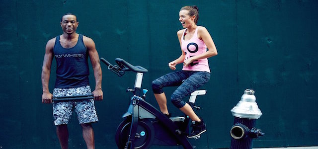 An athletic man and woman outside working out on a stationary spin bike.