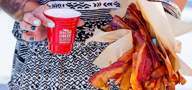 A woman with tattoos holding fresh crispy bacon and a red plastic cup of beer.