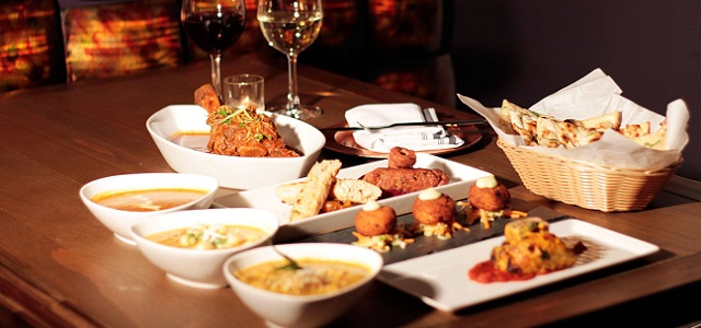 An asortment of appetizers and wine on a brown wooden table at Kurry Qulture in Astoria, Queens.