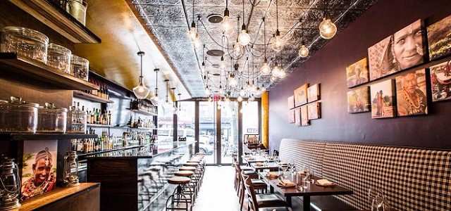 An interior view of Kurry Qulture's decor with upholstered booths, hanging lights and bulbs, and bright sunshine through a large window.