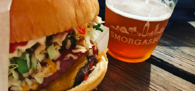 A fresh hamburger with colorful toppings with a plastic cup of beer at Smorgasburg.