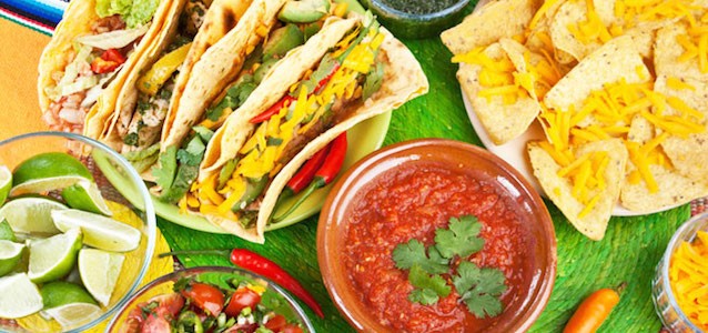 A spread of fresh and colorful taco toppings and vegetables with red salsa and green limes.