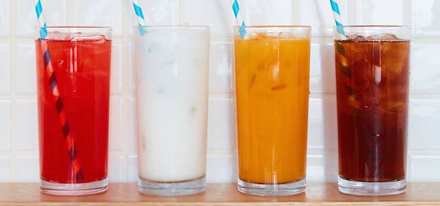 Four glasses with fresh juices and teas with blue and white striped straws on a wooden table.