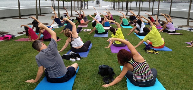 A group of people sitting outside at Roosevelt Island in NYC taking a yoga class.