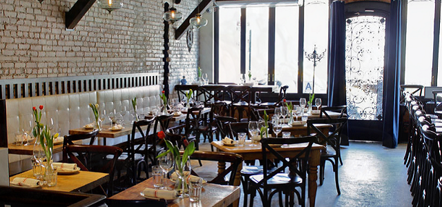 An interior view of Medi Wine Bar's rustic seating area with cushioned booths, dark wood tables, and large bright windows.