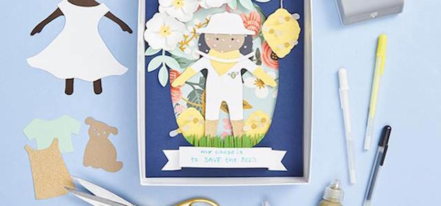 A paper card from Paper Source with dolls and markers on a light blue table.