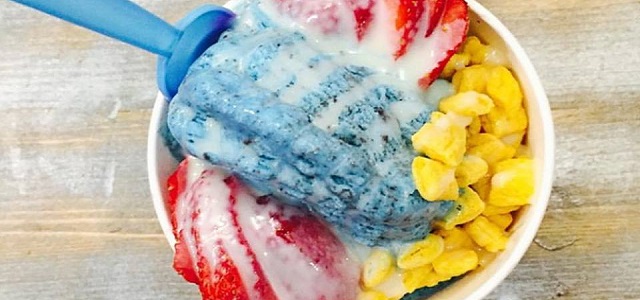 A cup of shaved ice cream with fresh yellow mango and red strawberries with a blue spoon.