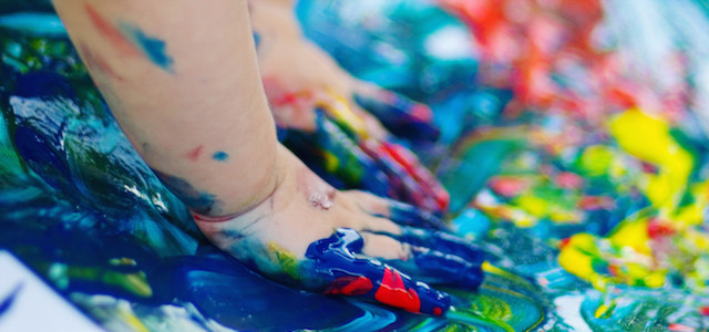 A toddler's hands finger painting with brightly colored rainbow paint.