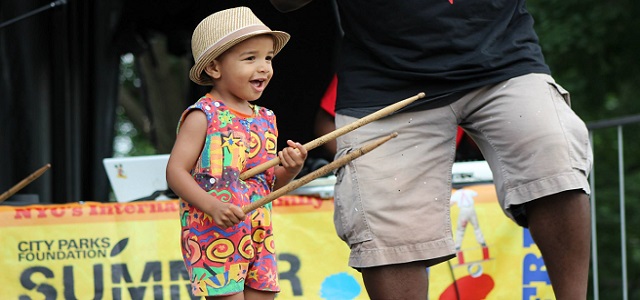 A little girl holding drum sticks on stage at SummerStage in Central park.