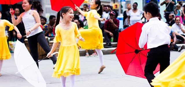 A group of children wearing brightly colored, traditional clothing dancing to Chinese music.