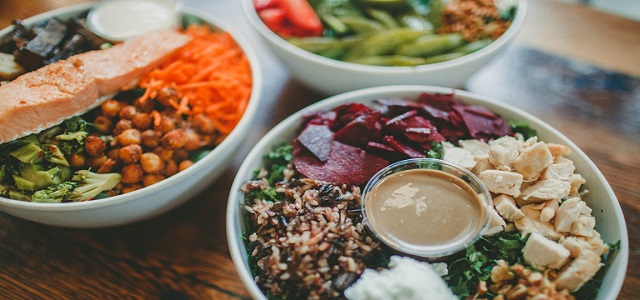 Three salad bowls on a table top with fresh ingredients and salad toppings.