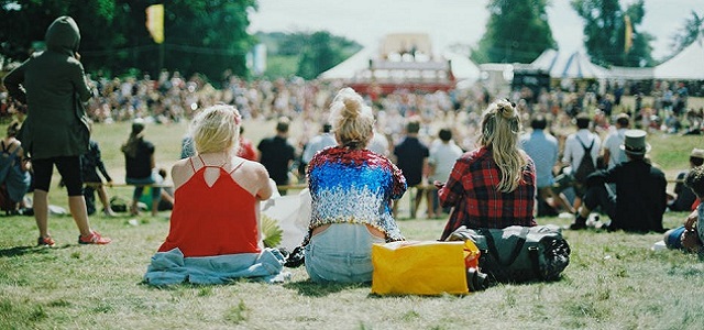 Girls sitting on the grass outside an an outdoor music concert.
