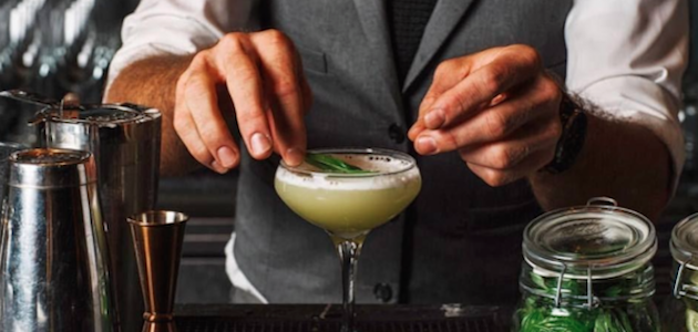 A bartender at American Cut handcrafting a green cocktail over ice in New York City.