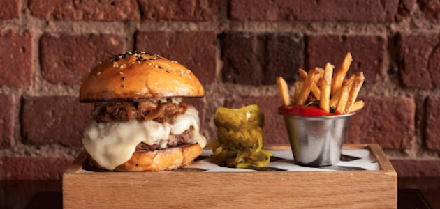 A freshly cooked cheeseburger and fries on a wooden table at American Cut in NYC.