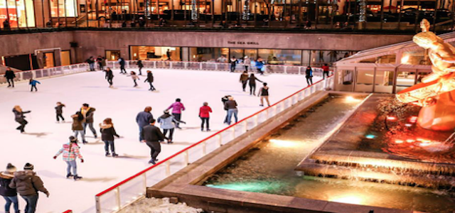 A group of ice skaters at Rockefeller Center's ice skating rink at night.