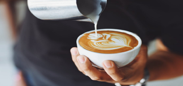 A man holding a cup of coffee and pouring milk into it as a design.