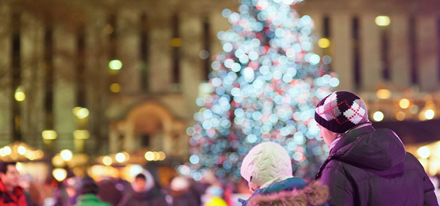 A father and son ice skating in New York City near a lit Christmas tree.